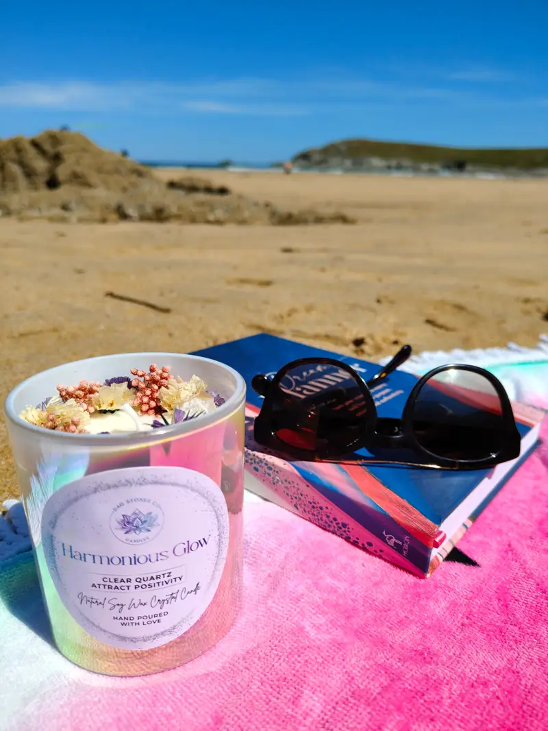 Harmonious Glow crystal candle by Dag Stones on a sandy beach with sunglasses and a book